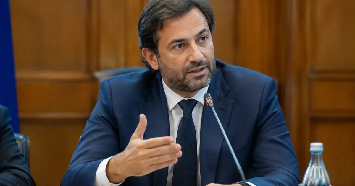 Uomo in completo seduto al tavolo parla al microfono
