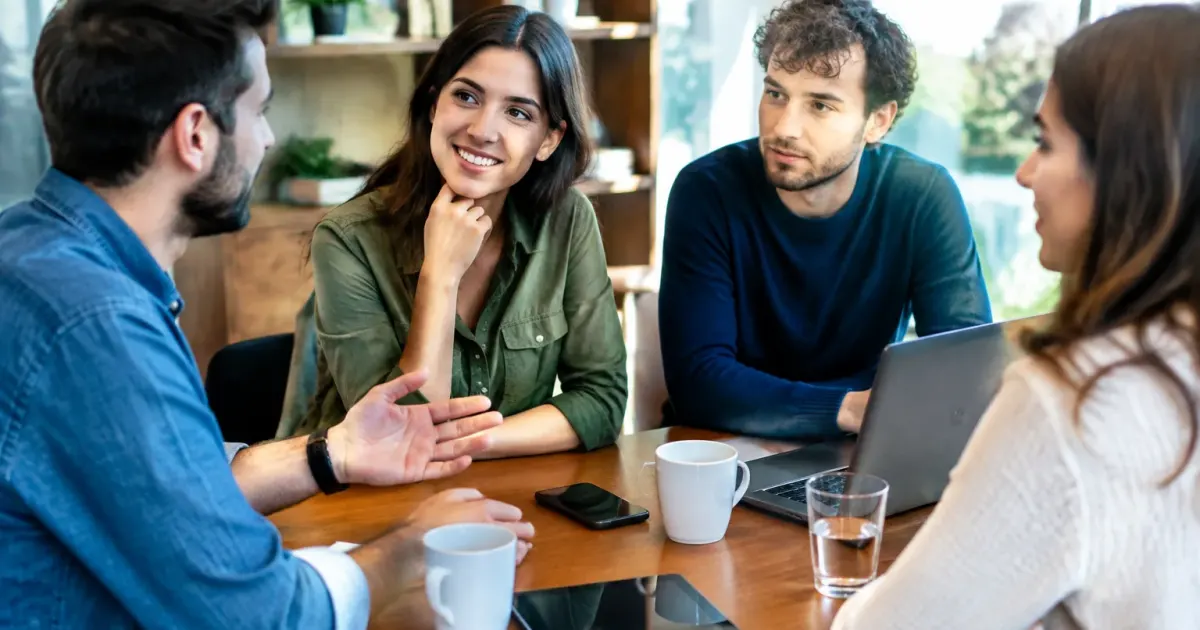 Persone sedute attorno tavolo conversano faccia a faccia
