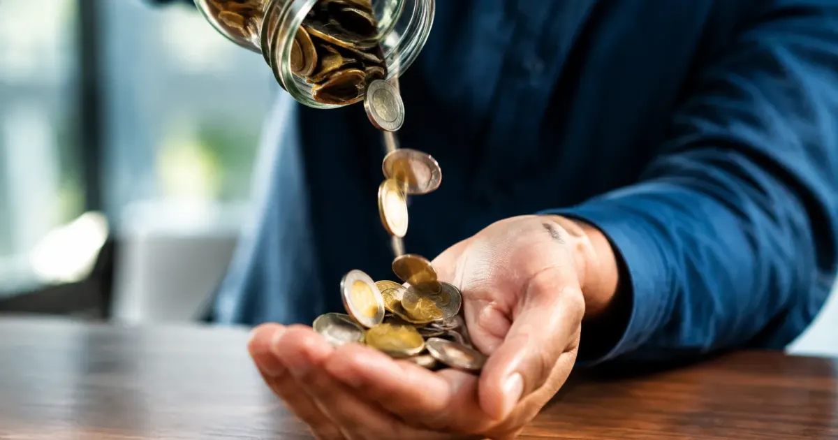 Persona tiene monedas cayendo en mano abierta sobre escritorio