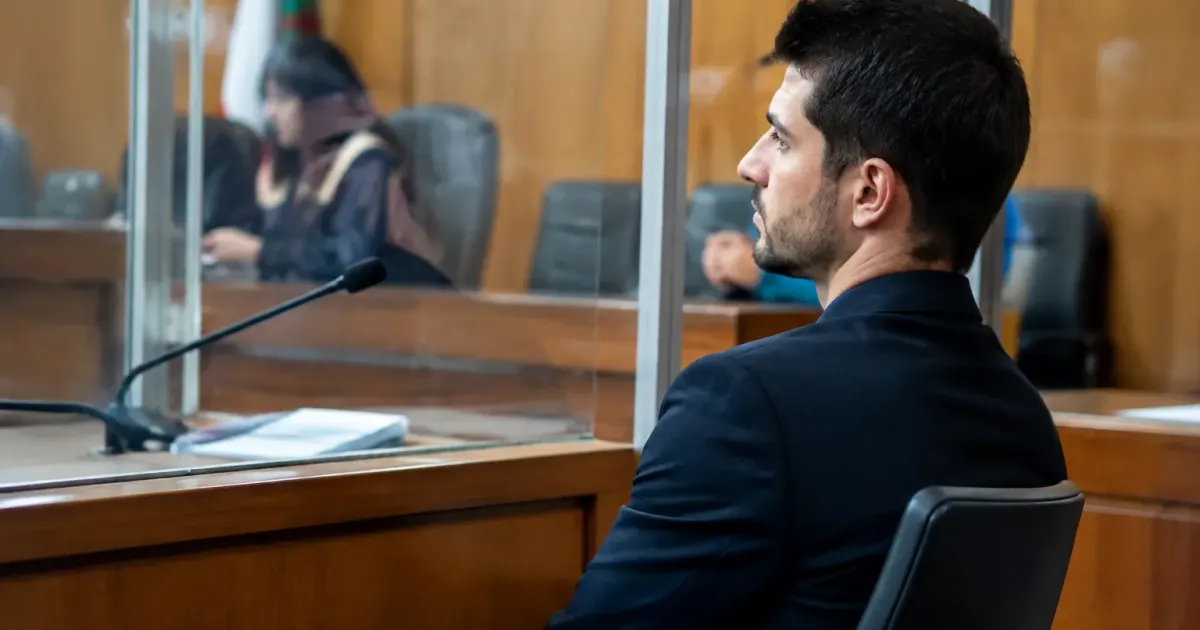 Uomo seduto dietro pannello vetro aula giudiziaria durante processo