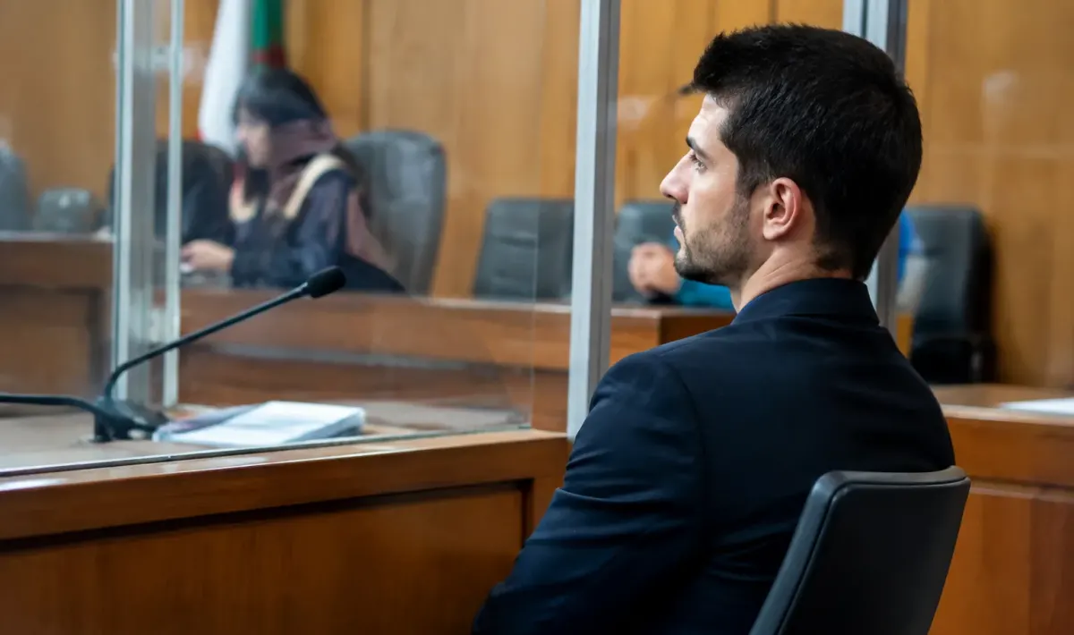 Uomo seduto dietro pannello vetro aula giudiziaria durante processo